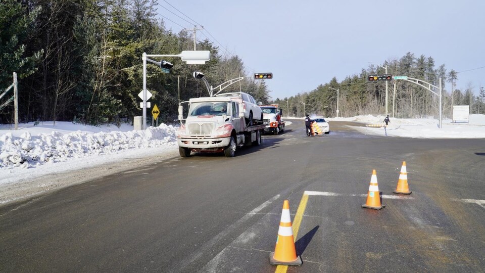 Une voiture sur un camion remorque et des policiers qui assurent la circulation.