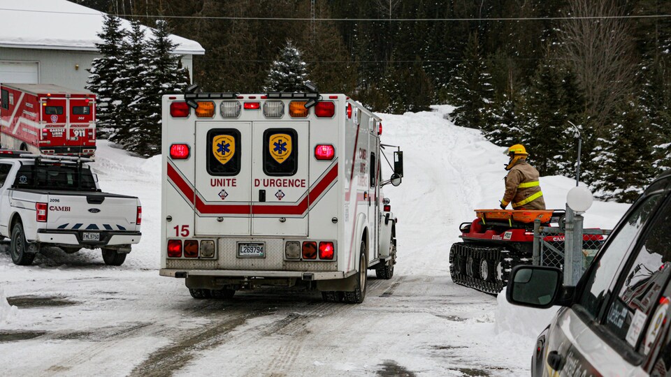 Un pompier debout dans un véhicule muni de chenilles, à côté d'une ambulance.