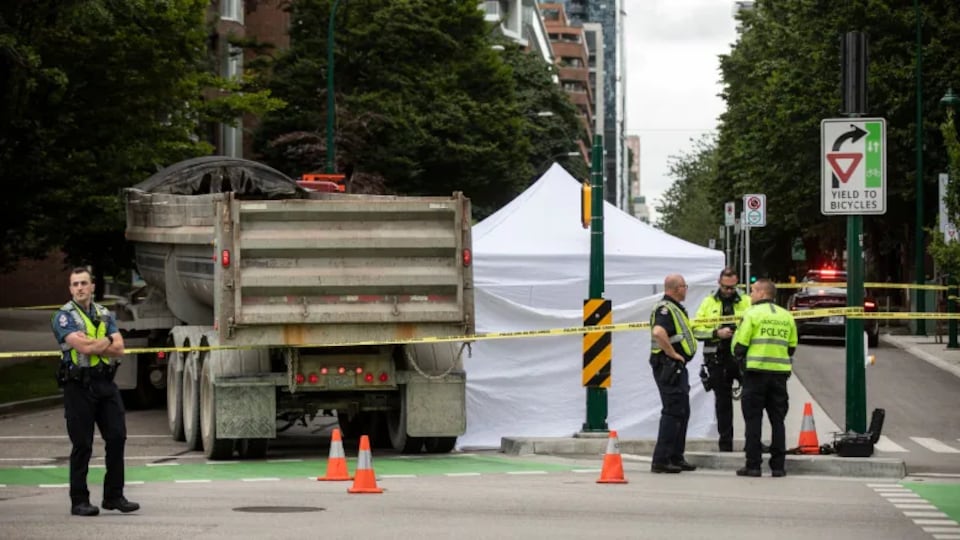 Des policiers protègent une scène avec un camion et une tente blanche à l'intersection d'une piste cyclable