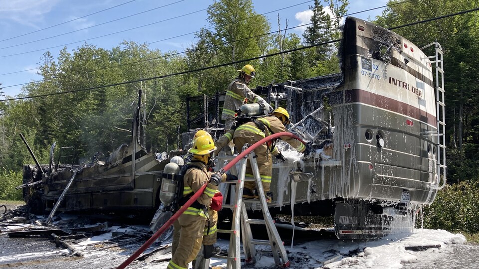 Un véhicule récréatif détruit est arrosé par les pompiers.