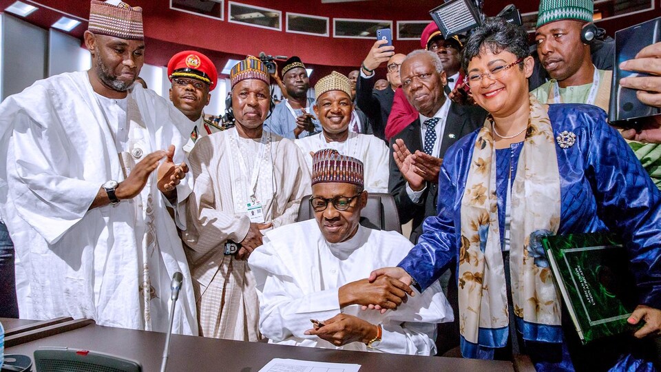 Muhammadu Buhari assis, une plume à la main, entouré de dizaines de représentants africains.