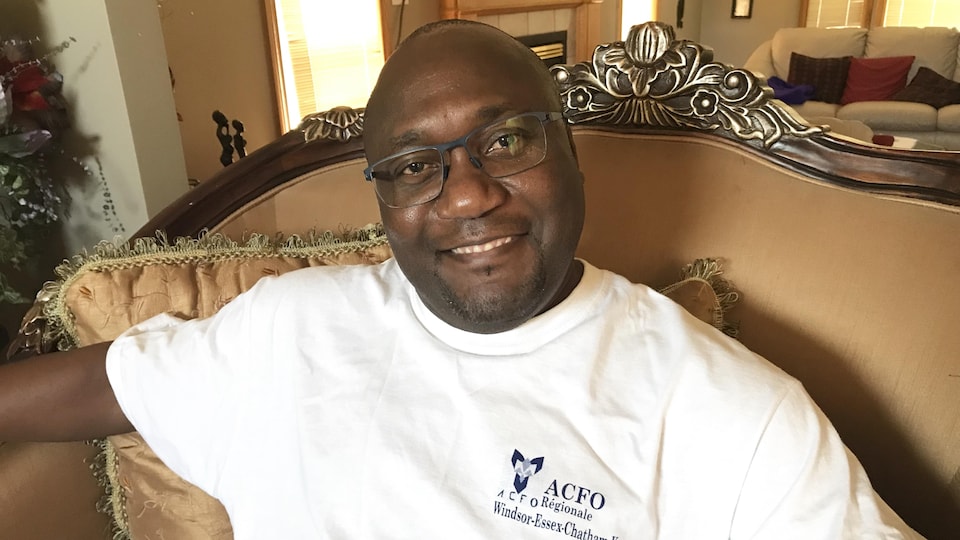 François Nono sits on a couch and wears a sweater on which he is inscribed ACFO Régionale Windsor-Essex-Chatham-Kent.