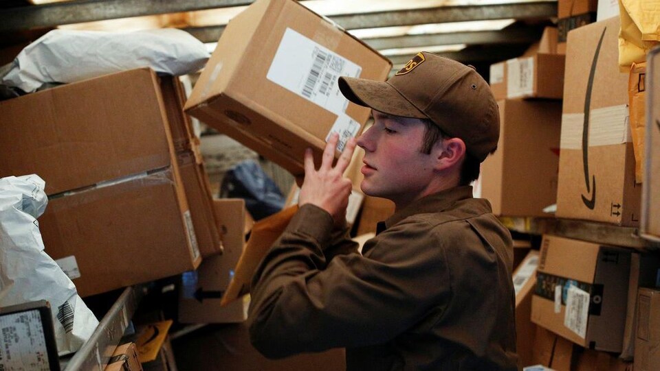 Photo d'un livreur de la compagnie UPS habillé en brun en train de soulever une boîte.