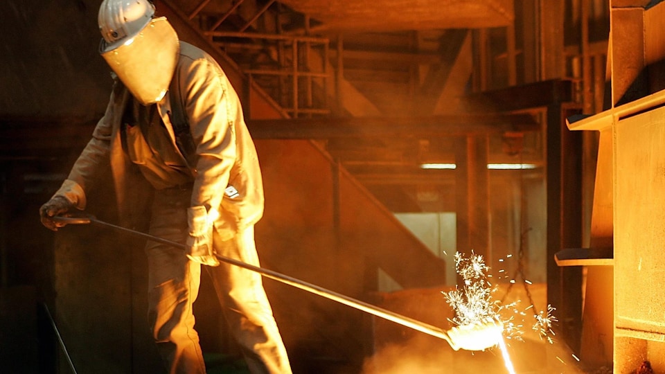 Un travailleur de l'acier habillé d'une combinaison manipule de l'acier en fusion.