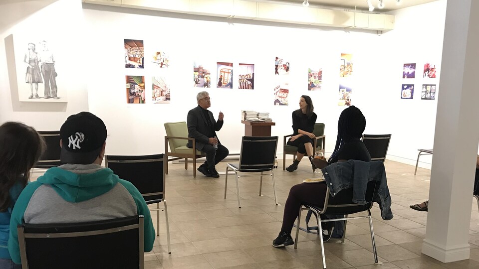 Des personnes distancées dans une salle d'exposition écoutent une discussion.
