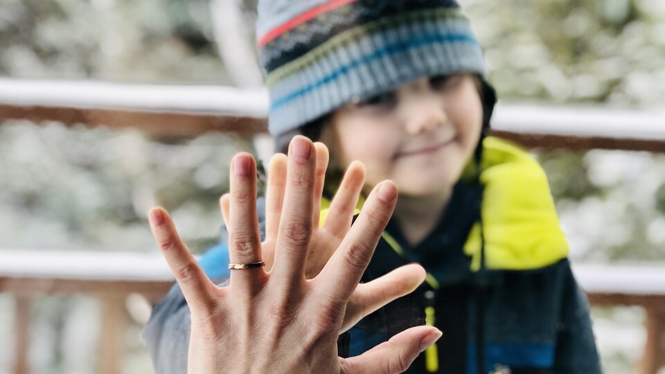 Un enfant met sa main dans celle d'un adulte à travers une fenêtre.