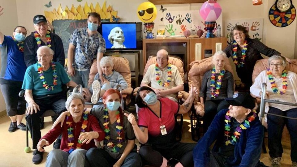 Des employés et des personnes âgées dans une salle commune portent des colliers fleuris de style hawaïen.