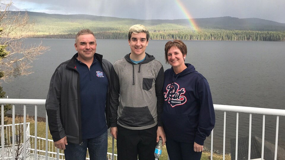 Adam Herold pose avec ses parents Russell et Raelene Herold, devant un lac.