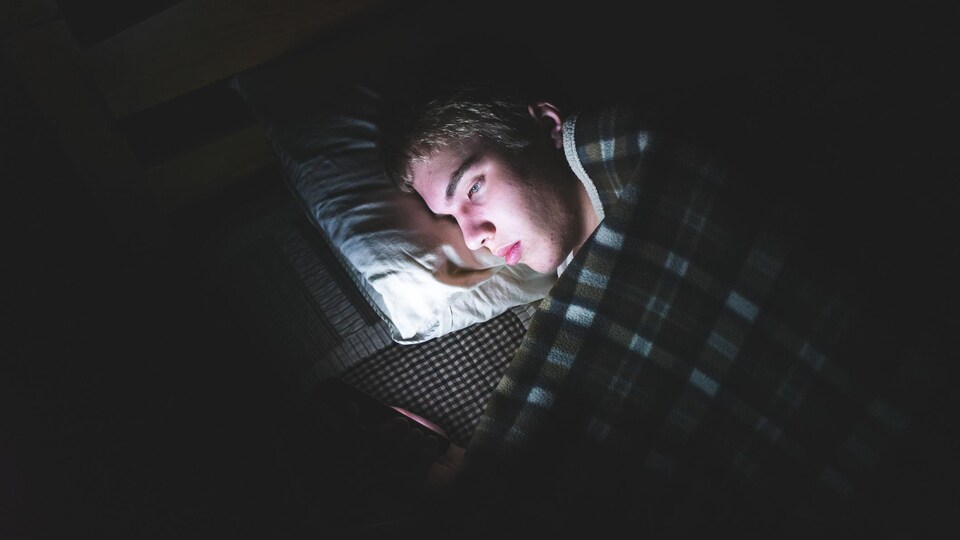 Un adolescent consulte son téléphone dans son lit.