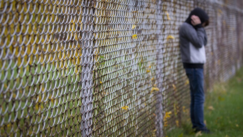 Un adolescent appuyé sur une clôture se bouche les oreilles.