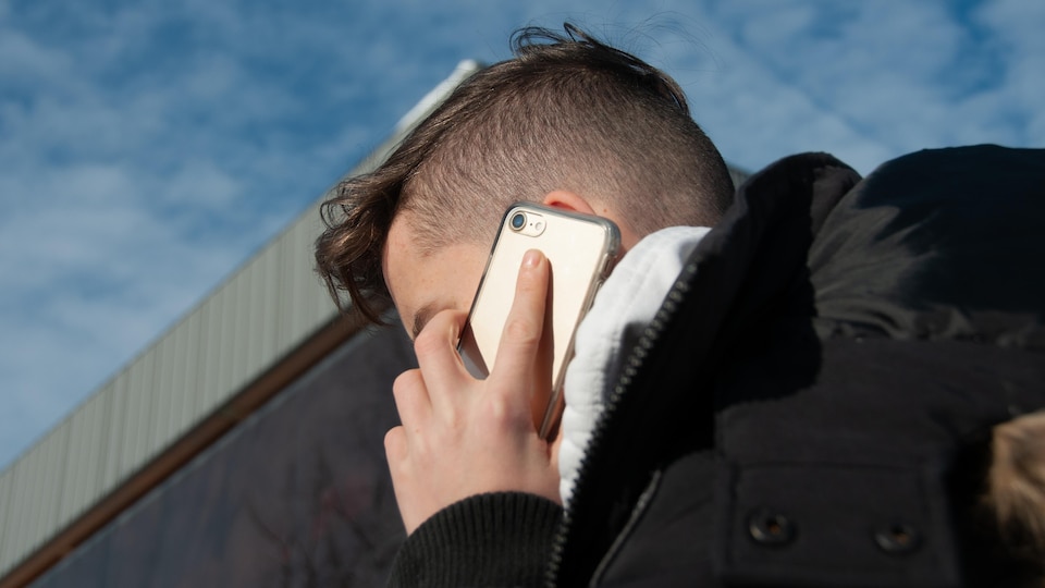 Un adolescent aux cheveux coupés très courts à la nuque, vu de profil, presse un téléphone cellulaire sur son oreille.
