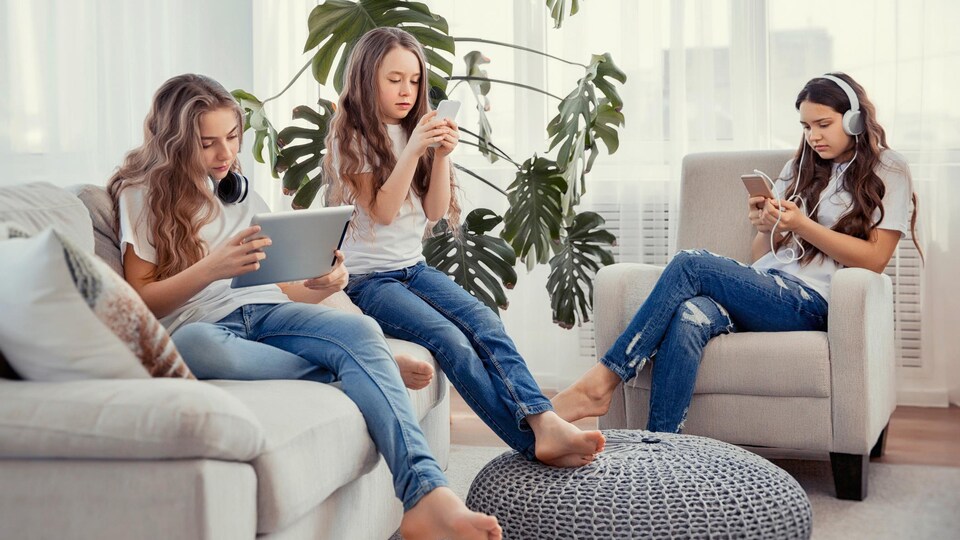 Trois jeunes filles utilisent des téléphones intelligents et une tablette pour écouter et regarder du contenu.