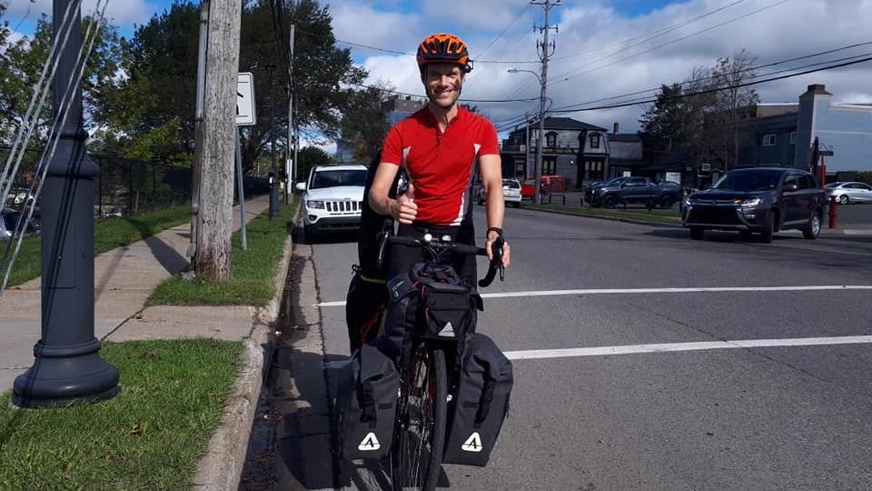 Adrian House sur sa bicyclette dans une rue résidentielle faisant un signe d'approbation du pouce.