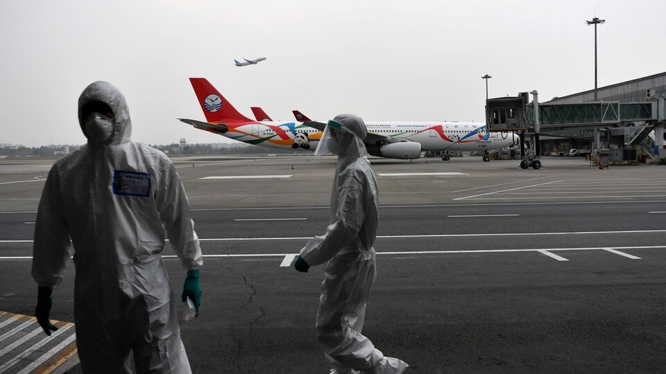 Deux hommes en combinaison et masqués sur le tarmac d'un aéroport.  
