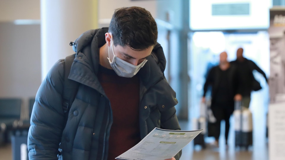 À son arrivée à l'aéroport Billy Bishop de Toronto, un voyageur consulte un dépliant de santé concernant la COVID-19.