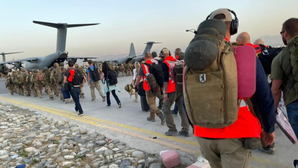 Une file de passagers et de militaires sur le tarmac de l'aéroport de Kaboul se dirigeant vers des avions.