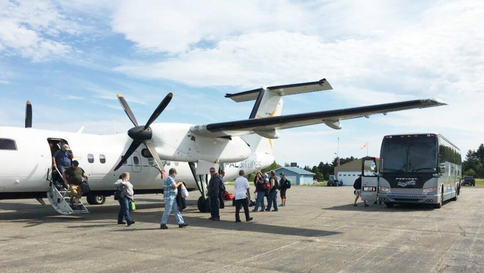 Des passagers sortent d'un avion et se dirigent vers un autobus, sur la piste de l'aéroport de Matane.