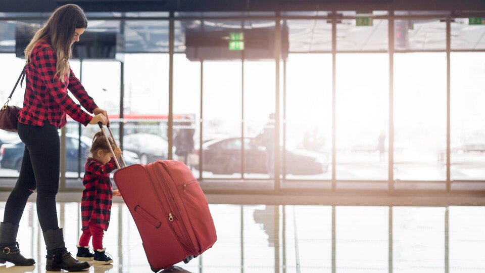 Une mère et sa fillette poussent leur valise dans un aéroport.