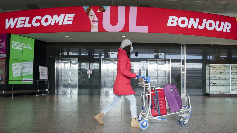 Une femme masquée pousse un chariot à l'aéroport de Montréal.