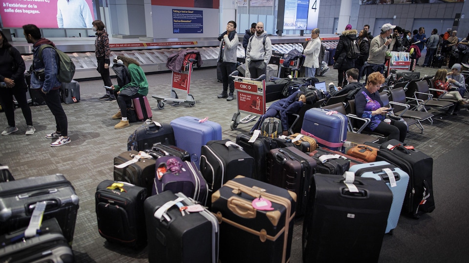 Des passagers attendent en ligne à l'aéroport Pearson près d'une vingtaine de valises.