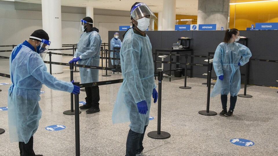 Des travailleurs portant masque, visière, gants et tenue de protection au centre de dépistage de l'aéroport Pearson.