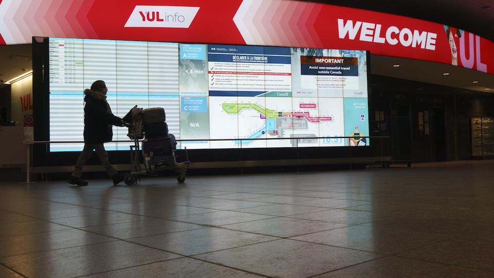 Un passager marche devant un tableau lumineux à l'aéroport Pierre-Elliott-Trudeau.