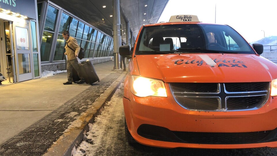 Un homme qui sort d'un taxi avec des valises se dirige vers l'entrée de l'aéroport.
