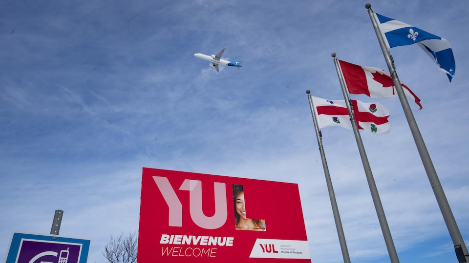 Des drapeaux, une grande pancarte sur laquelle est écrit YUL et un avion dans le ciel. 