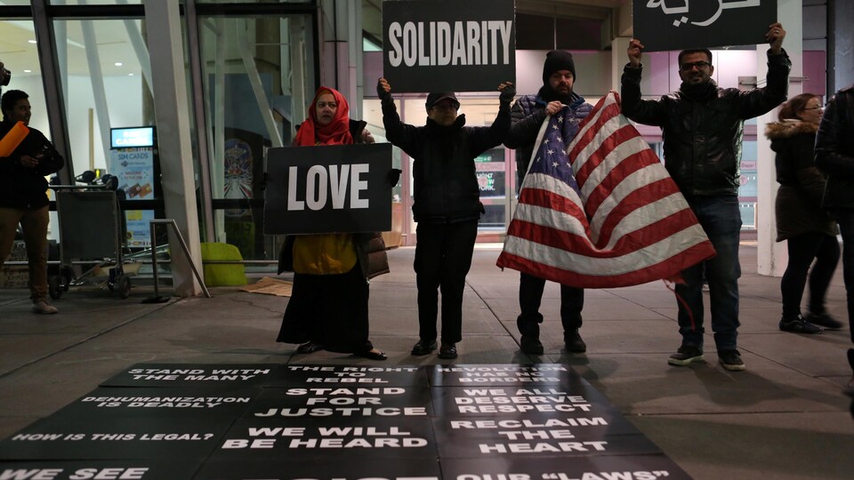 Des manifestants tiennent des pancartes appelant à l'ouverture, durant une manifestation spontanée à l'aéroport JFK à New York, samedi.