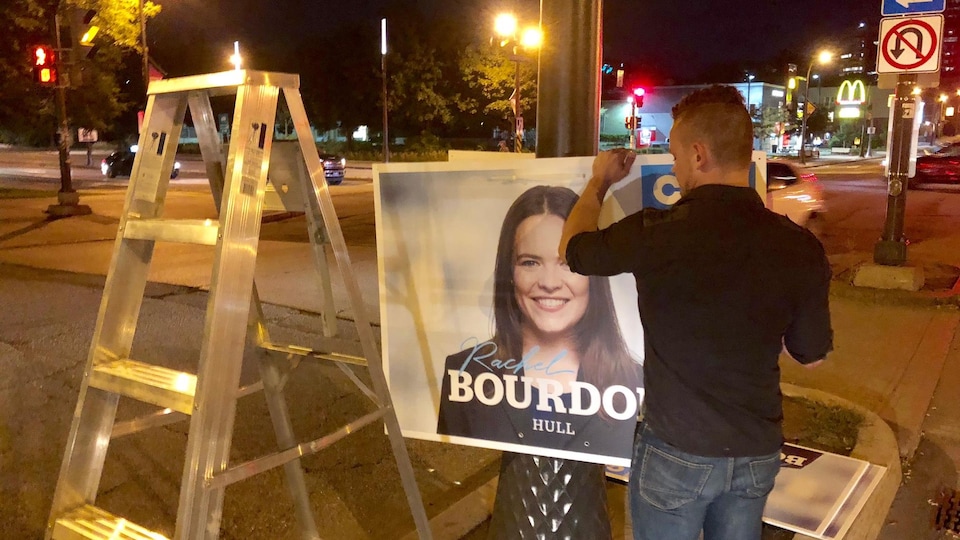 Un homme installe des affiches de la Coalition Avenir Québec sur un poteau dans une rue du secteur Hull à Gatineau.