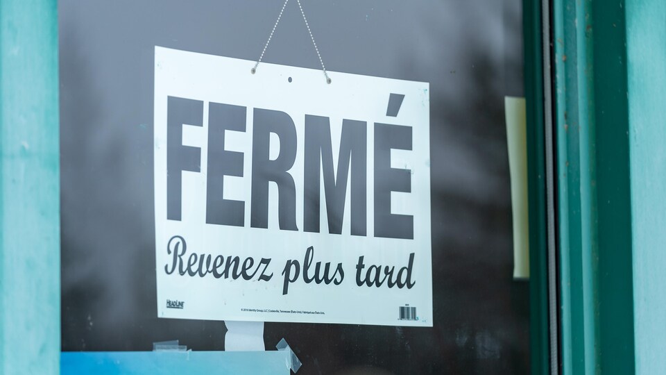 Une affiche sur laquelle on peut lire « fermé » et « revenez plus tard » dans la porte d'un commerce non identifié.