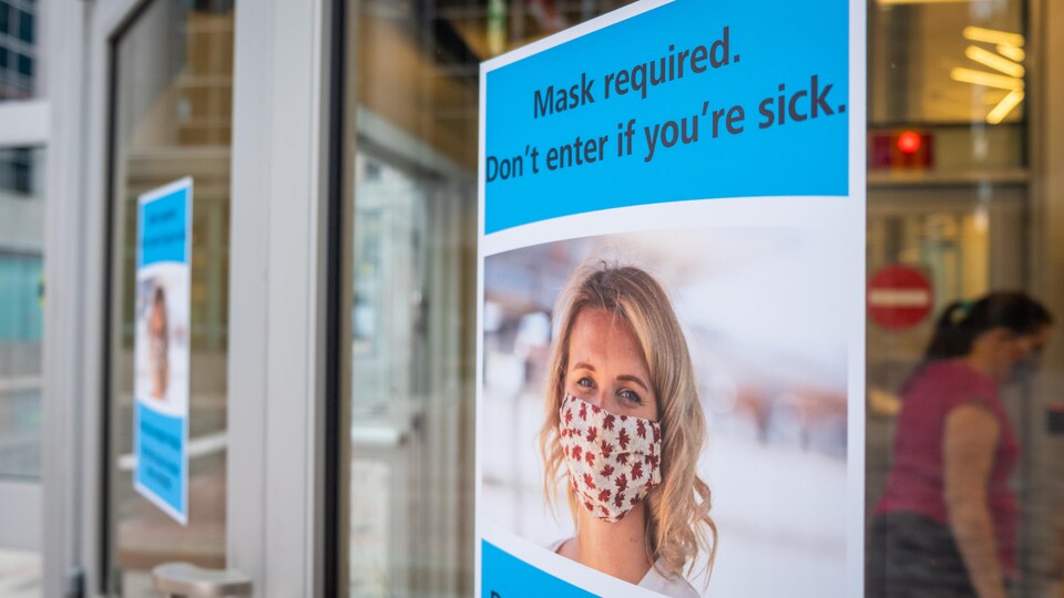 Une affiche montrant une femme portant un masque apposée sur une porte d'une station du train léger d'Ottawa.