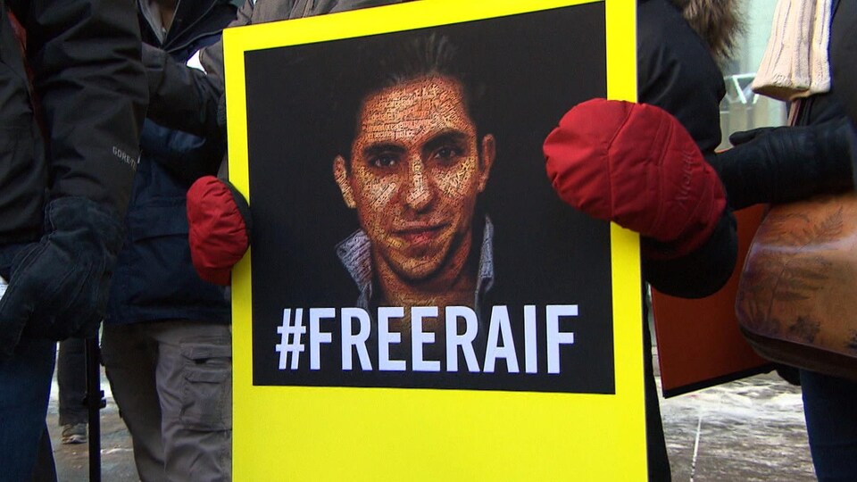 Une affiche montrant Raif Badawi, tenue par une personne.
