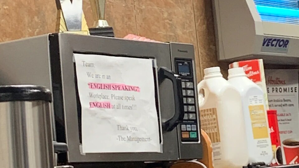 Une affiche posée sur un micro-ondes dans une cuisine de restaurant. L'affiche porte la mention : « We are an "English speaking" workplace. Please speak english at alll times!!!! »