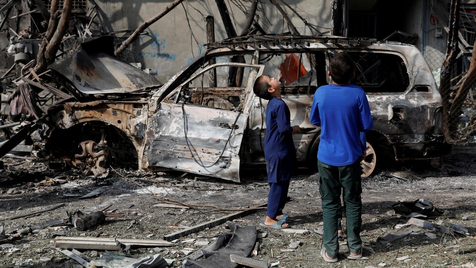 Des enfants devant une voiture calcinée et un immeuble endommagé par une explosion terroriste.