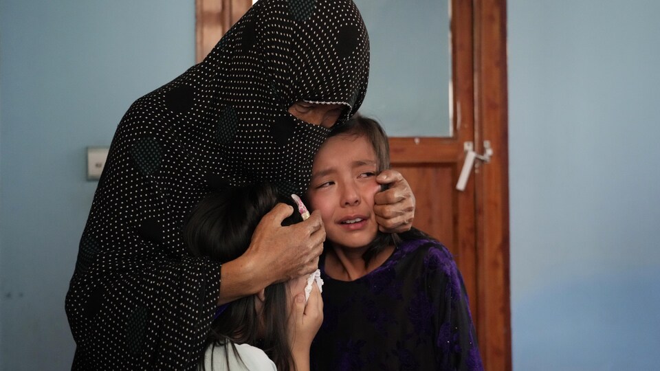 Une femme voilée tient dans ses bras deux jeunes filles en pleurs.