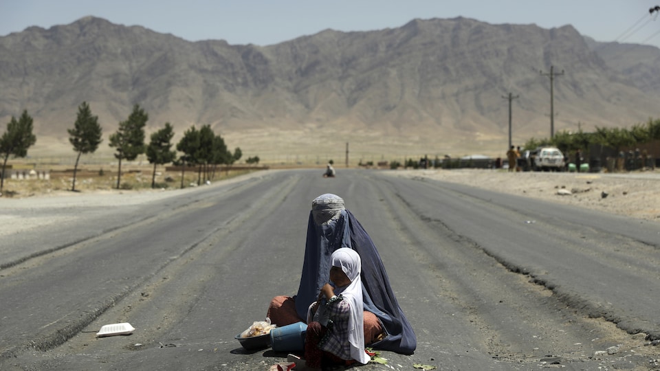 Una mujer con velo sentada en medio de la calle con un niño.