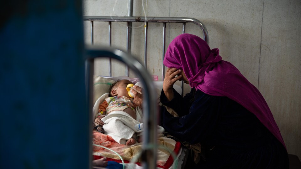 Une Afghane exténuée nourrit au biberon son bébé alité.