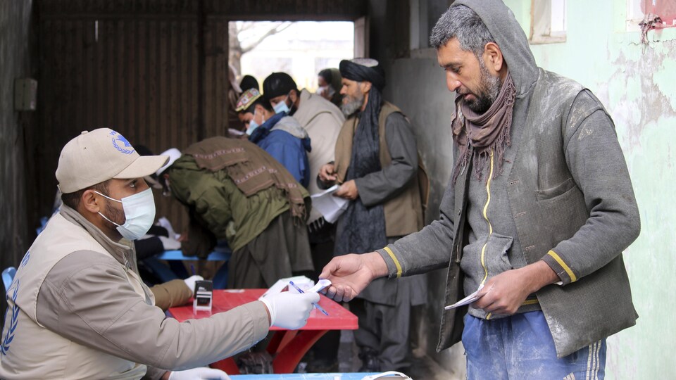 Un homme portant un masque offre un bon de nourriture à un homme.   - afghanistan famine - UKRAINE : La guerre risque de créer une crise alimentaire mondiale sans précédent.
