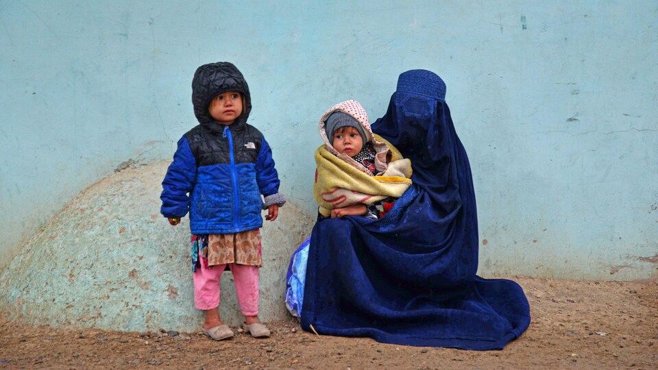 Une femme portant une burqa tient un enfant dans ses bras et se trouve près d'un autre.