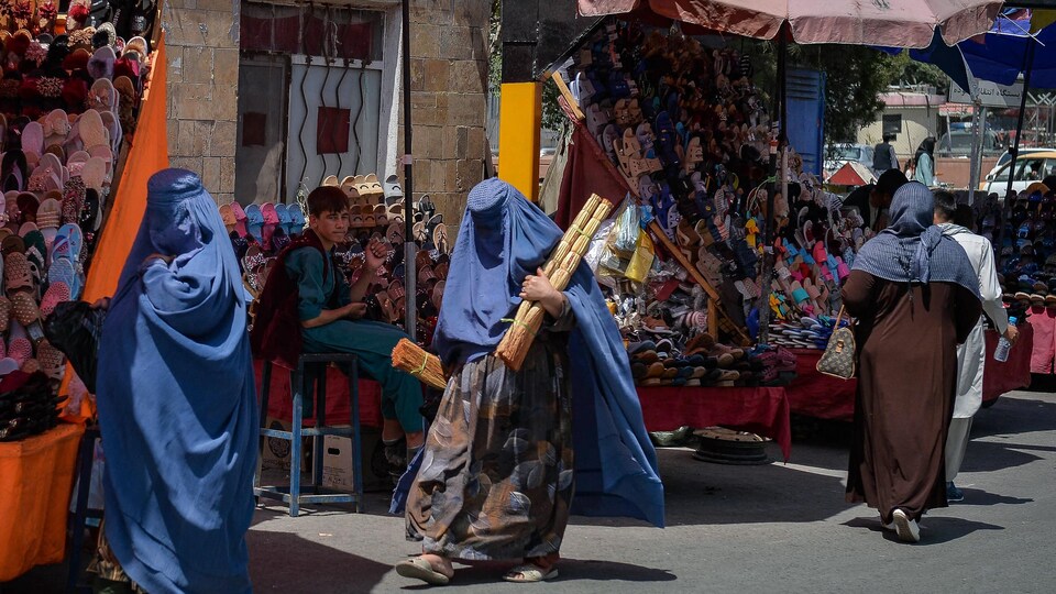 Deux femmes en burqa marchent près de petits commerces.