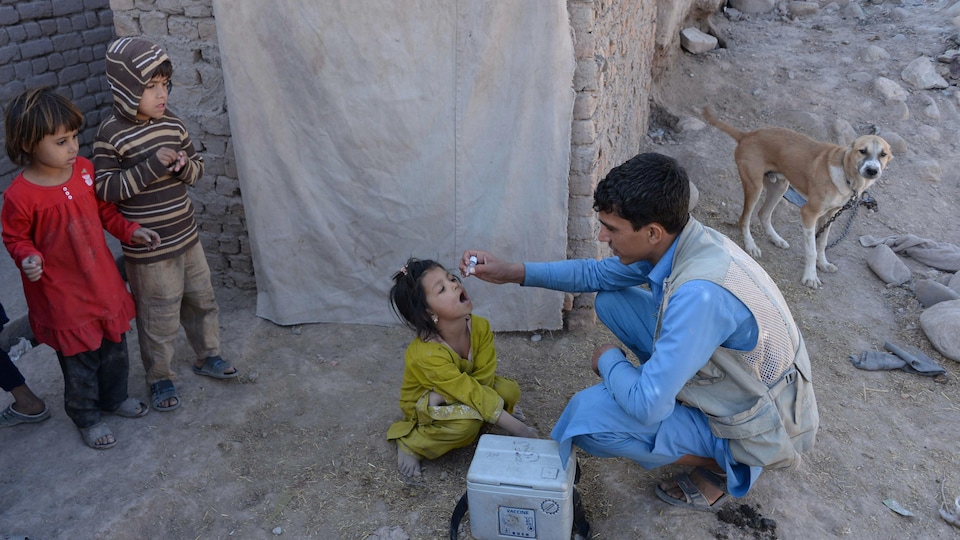 Une fillette accroupie par terre reçoit une dose de vaccin oral.