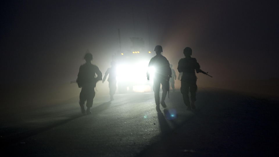 La silhouette de soldats vue devant les phares d'un véhicule.