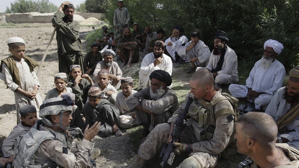 Des villageois afghans et militaires américains sont assis par terre et discutent.