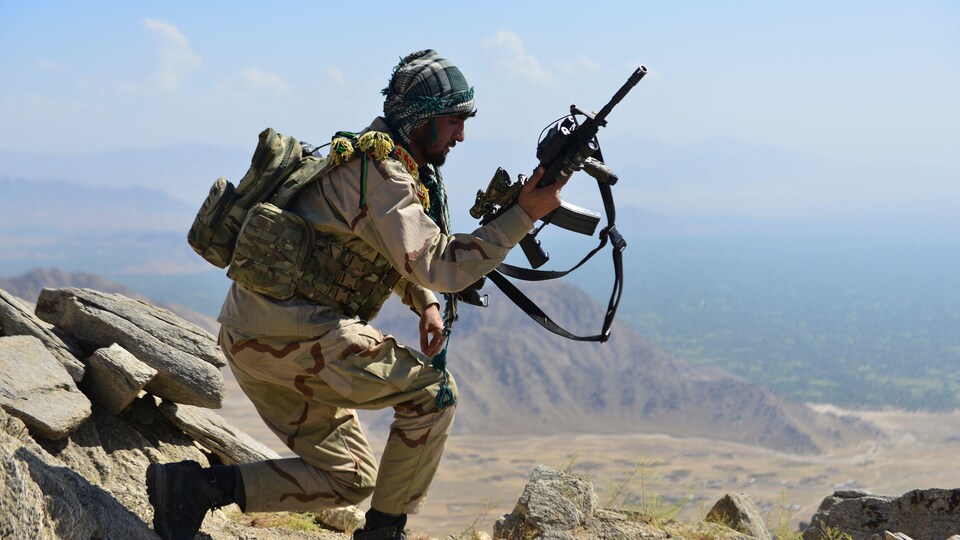 Un homme se promène sur le sommet d'une colline, un fusil d'assaut dans les mains.