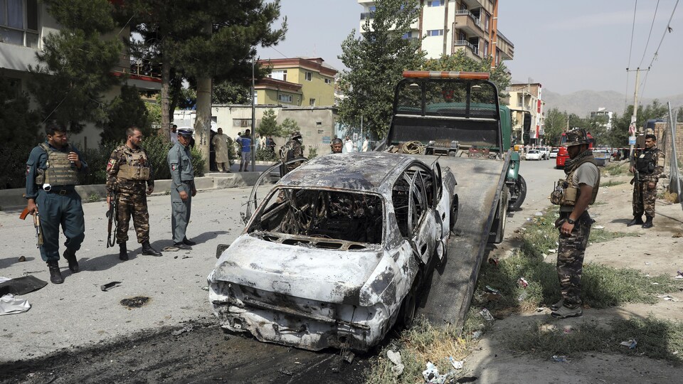 Des membres du personnel de sécurité afghan inspectent un véhicule endommagé.