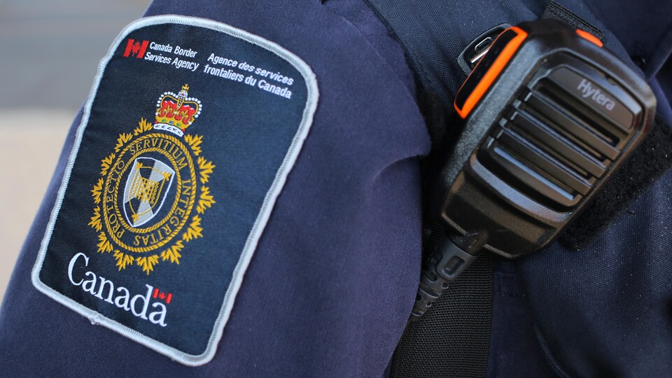 Écusson d'un agent de l'Agence des services frontaliers du Canada, qui porte également un émetteur-récepteur portatif.