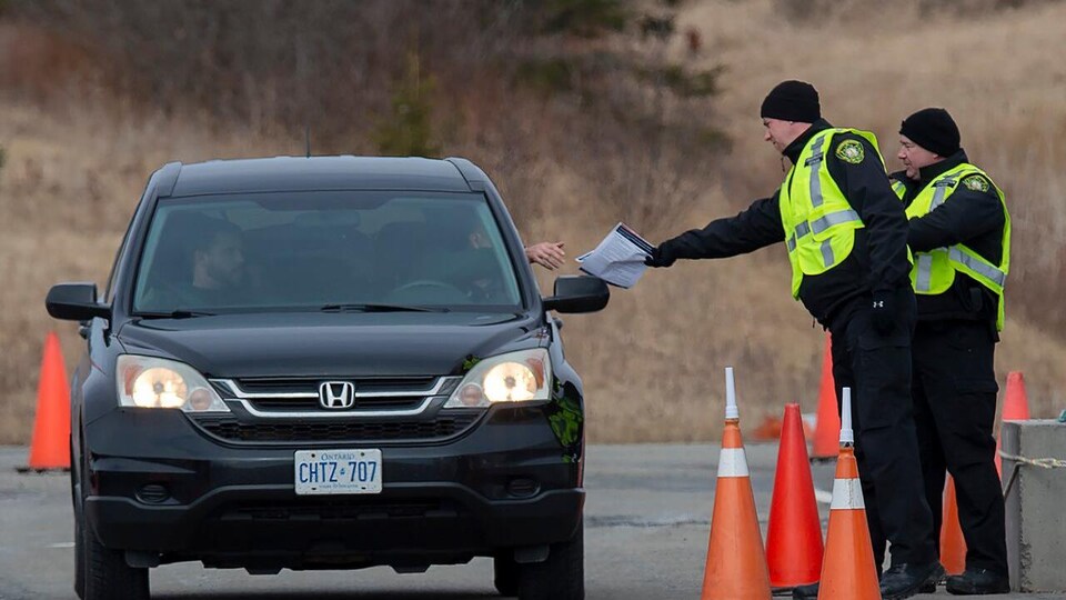 Deux agents près d'une voiture semblent vérifier des papiers appartenant au conducteur.