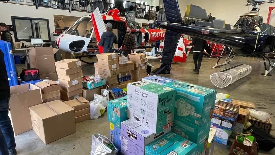 Des personnes dans un entrepôt avec deux hélicoptères et des boîtes de denrées non périssables.