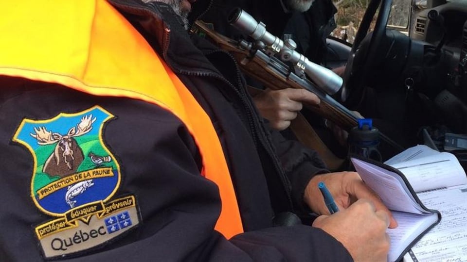 Deux hommes dans une voiture. Le premier remplit un constat d'infraction. Le second tient une arme..